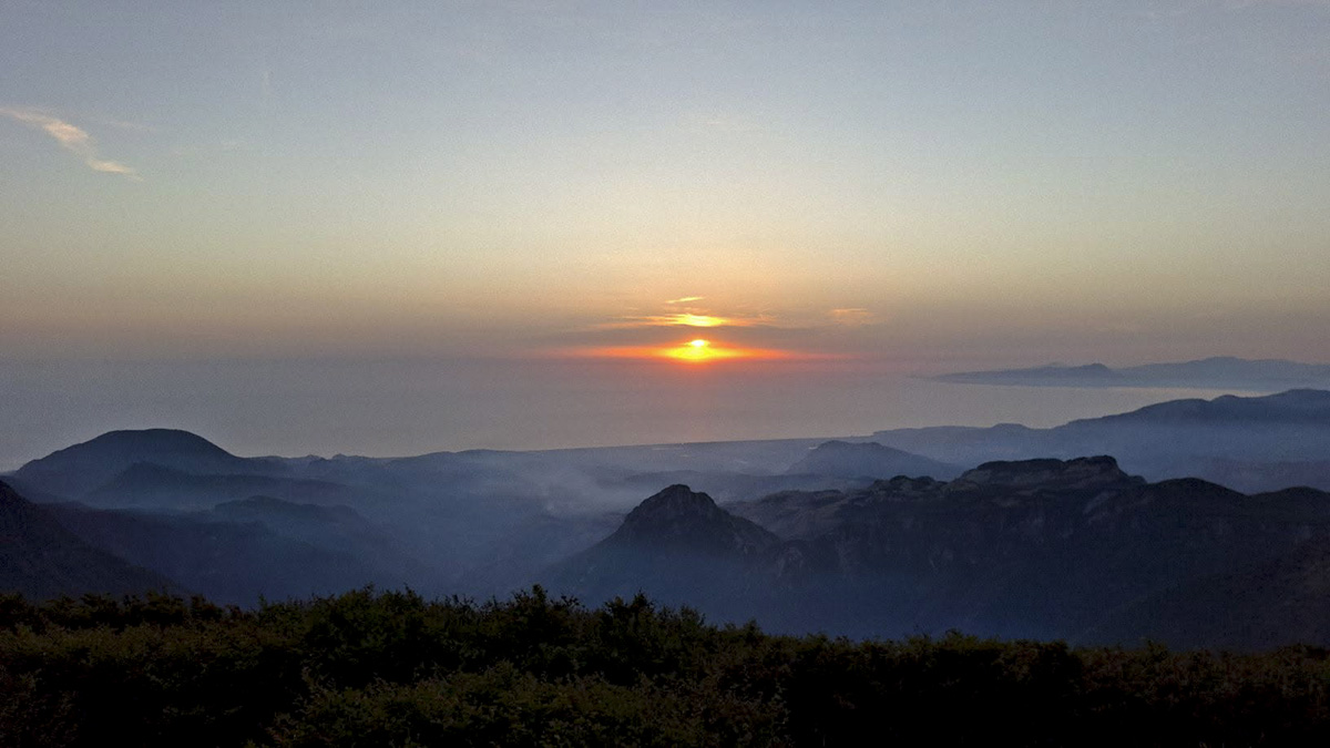 Panorama al tramonto dall'anticima del Cozzo del Pellegrino con il sole che scende sul mare e profili di montagne avvolti dalla foschia &copy;Francesco Cofone