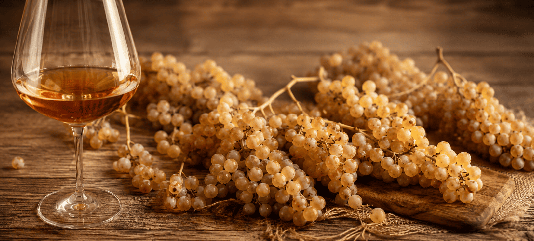 Calice di vino passito accanto a grappoli di uva Moscato di Saracena su legno